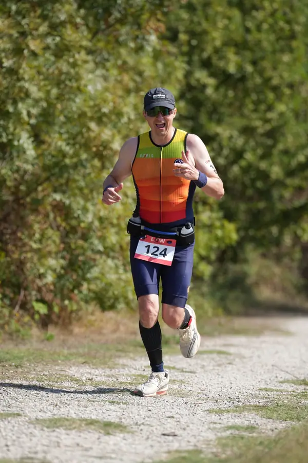 Course à pied, de près : Tiago Mance court tout sourire, en casquette et lunettes de soleil, le dossard sur sa ceinture porte-bidons.