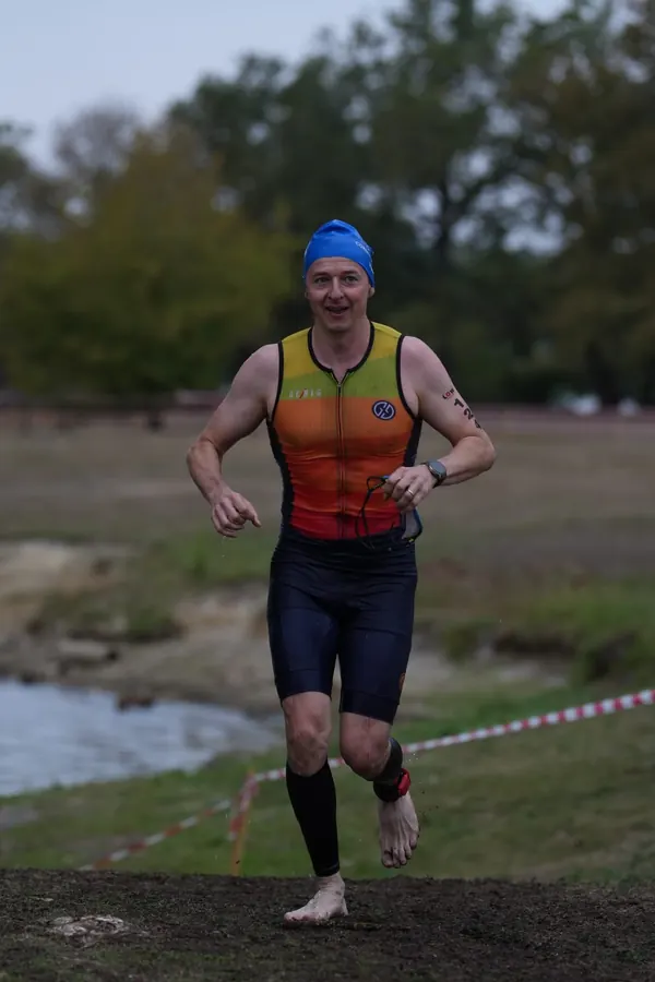 Triathlon, sortie de l'eau : Tiago Mance court pieds nus, en bonnet de bain bleu, la berge et une rubalise rouge et blanche derrière lui.