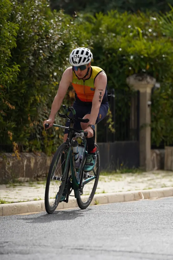 À vélo : Tiago Mance roule en casque blanc et lunettes de soleil, le long d'une haie et d'un portail.